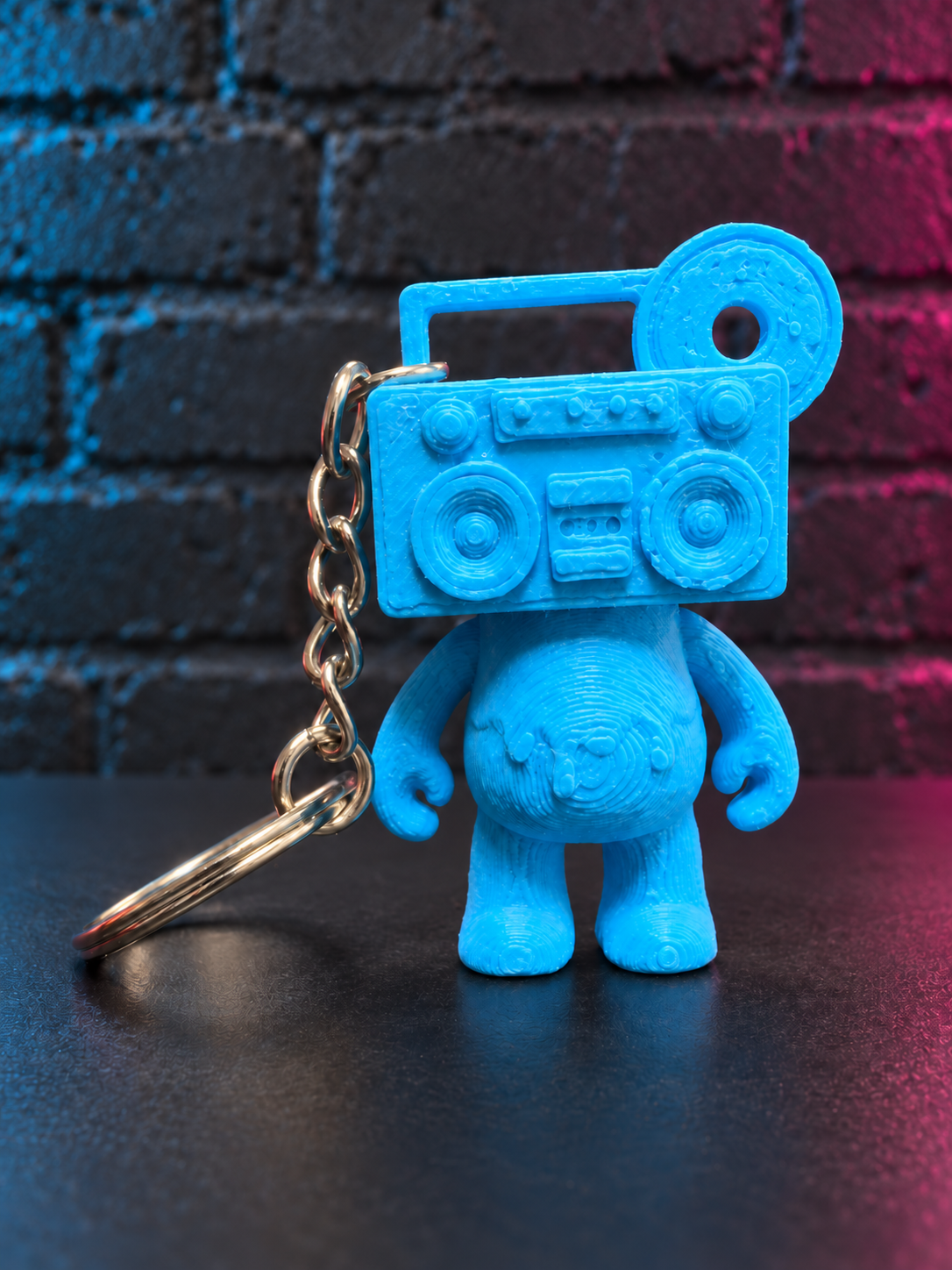 Boom Blue Boom Bear Mixtape Head keychain against a charcoal brick wall with subtle cyan and magenta lighting