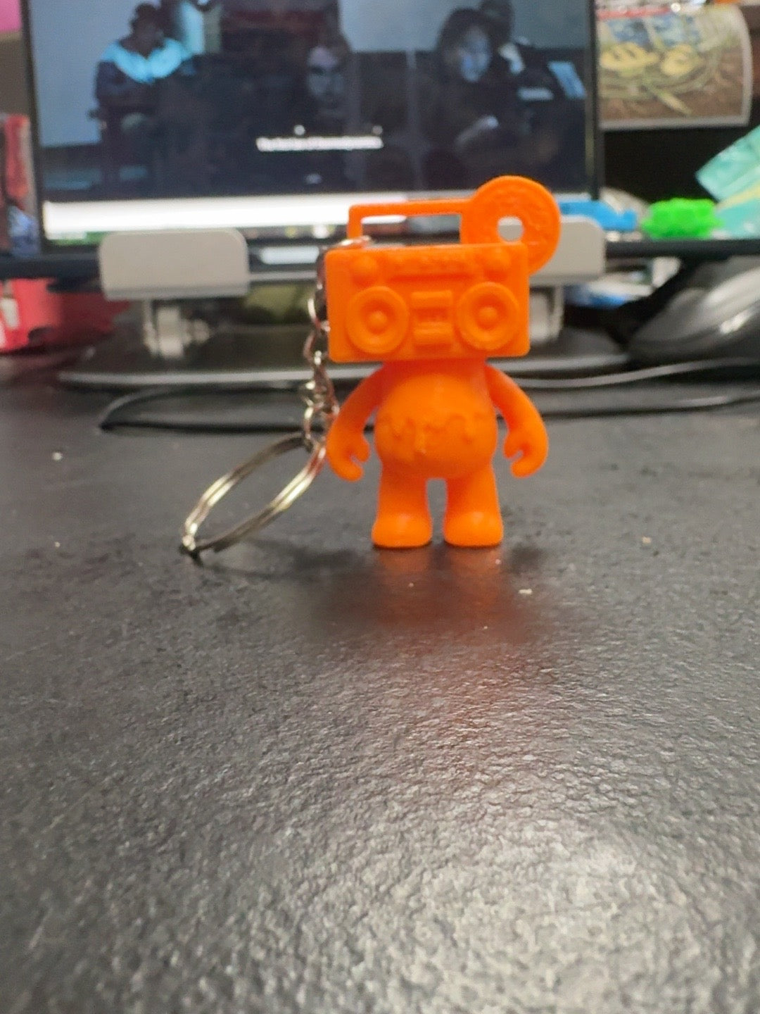 Front view of the Electric Orange Boom Bear Mixtape Head keychain standing on a black surface
