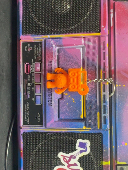 Electric Orange Boom Bear Mixtape Head keychain displayed on a colorful painted boombox
