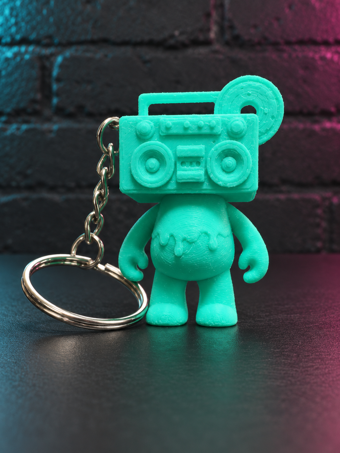 Fresh Mint Boom Bear Mixtape Head keychain against a charcoal brick wall with subtle cyan and magenta lighting