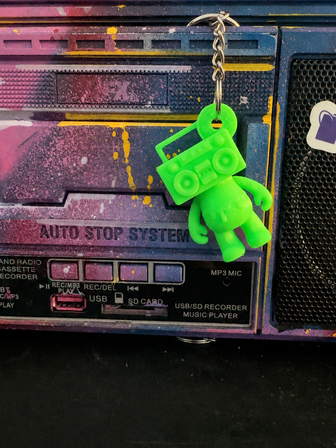 Neon Green Boom Bear Mixtape Head keychain hanging from a colorful painted boombox