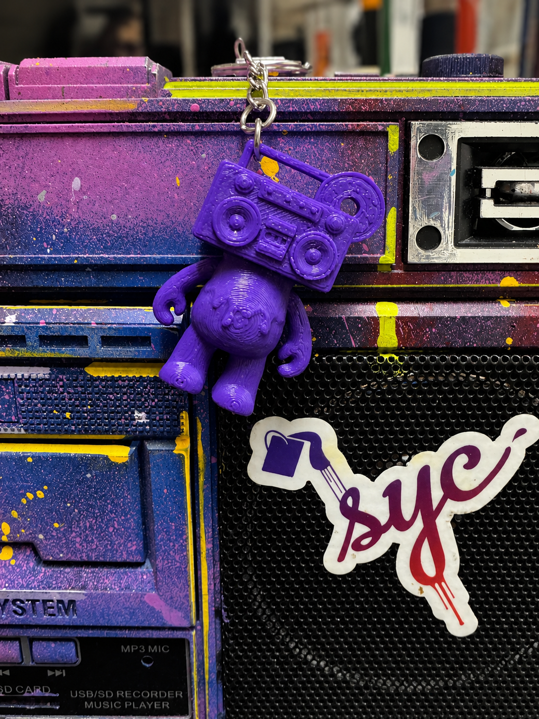 Remix Purple Boom Bear Mixtape Head keychain hanging from a colorful painted boombox beside the SYC sticker
