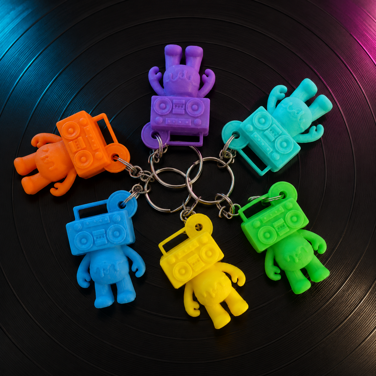 Six colorful Boom Bear Mixtape Head keychains arranged on a black vinyl record with cyan and magenta studio lighting