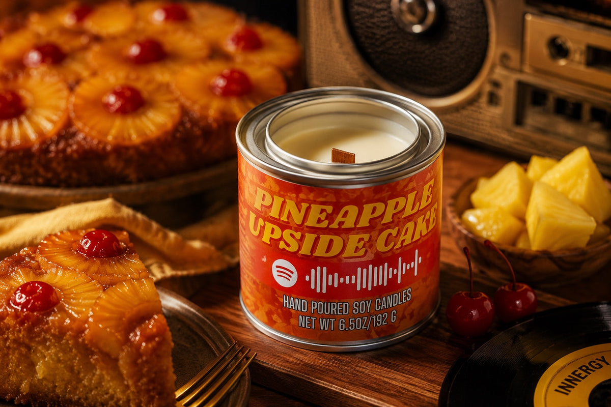 Pineapple Upside Down Cake Mixtape Candle unlit with wooden wick beside pineapple cake, fruit, and retro music styling.